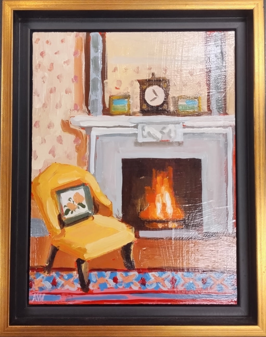 An oil painting in a gold and black frame of a cozy fireplace scene. The fire is bright orange and roaring inside a white mantle, with paintings and a clock on the mantle. A golden yellow chair is in the left corner with a pillow on it and a colorful rug is in the foreground. 
