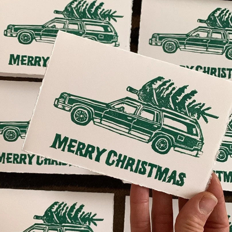 relief linocut greeting card featuring a car with a christmas tree on top with "Merry Christmas" written beneath the car