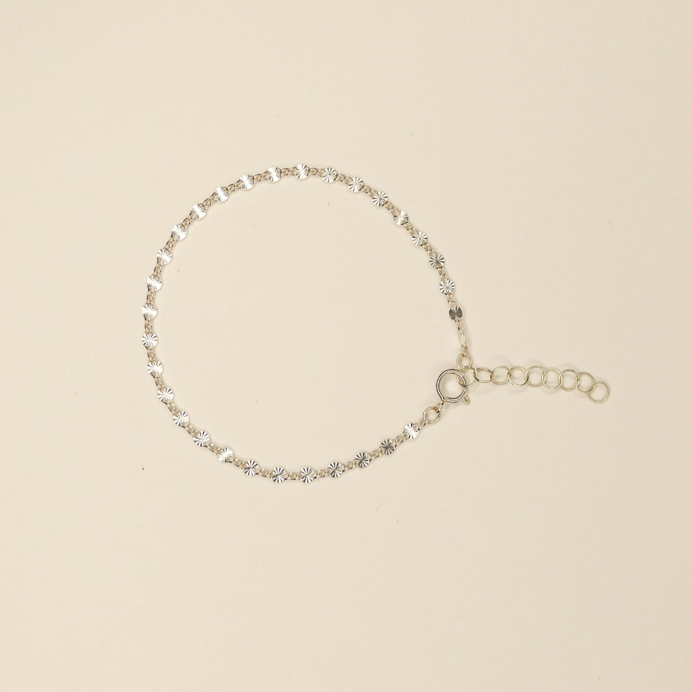 Delicate tiny flat ridged connecting disks make up this shimmery bracelet. Pictured on an off white background. 