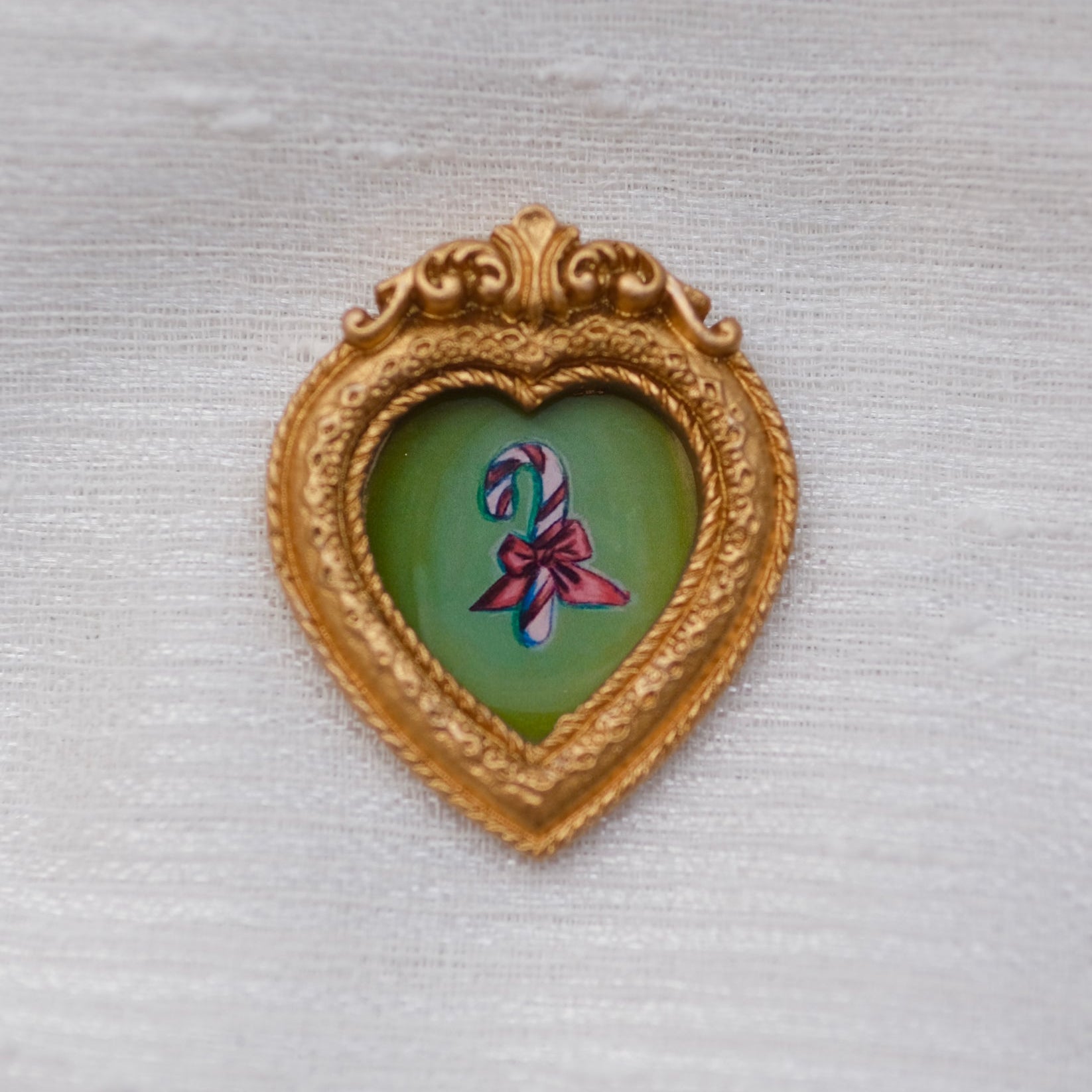 A painting of a candy cane with bow tied around it in a framed magnet. 