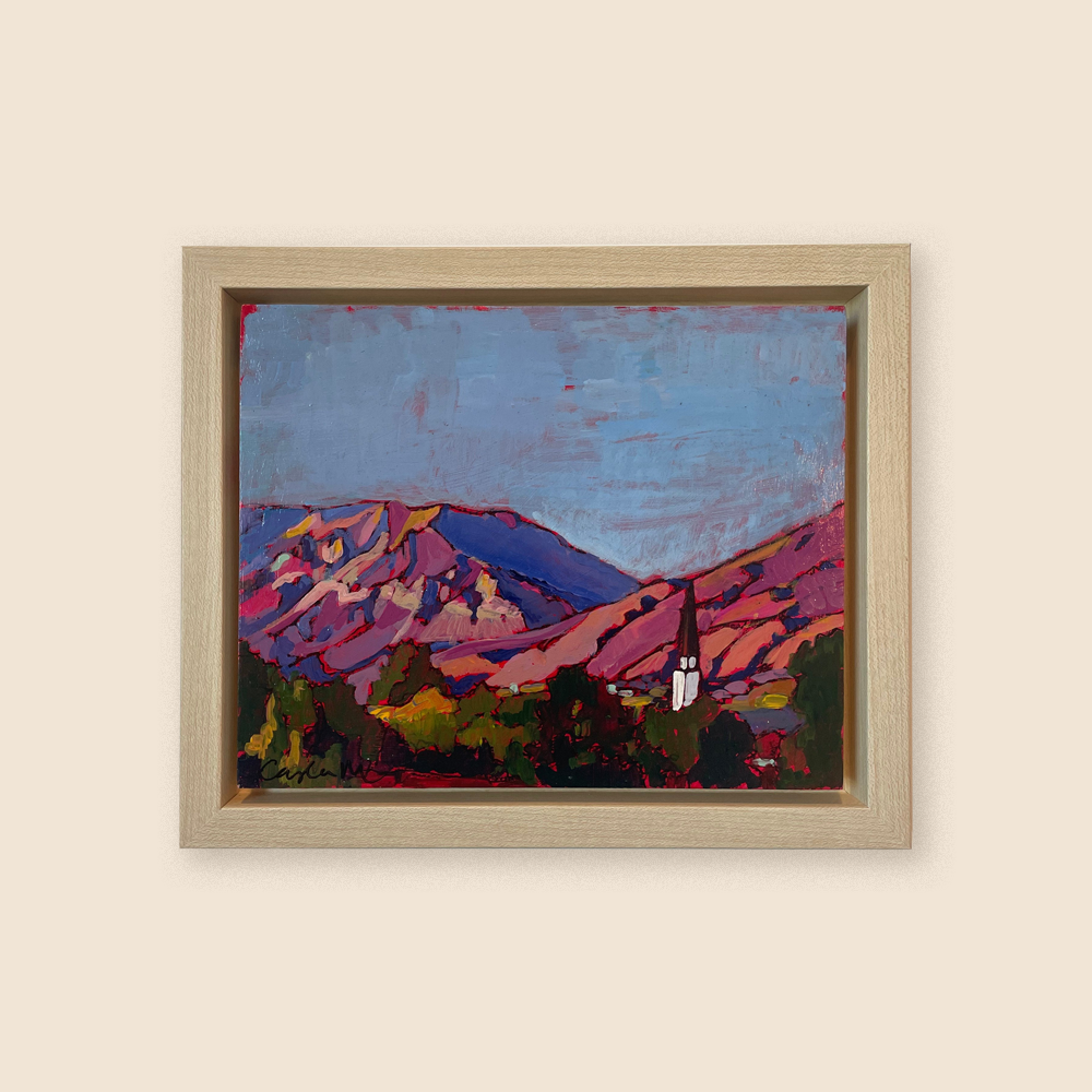 A white and red steeple poking out of green trees among a dusky hued pink and red mountain scape. 