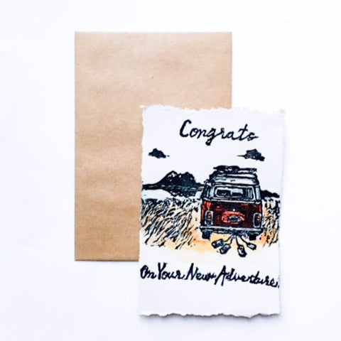 4x6 hand carved and pressed card reading "Congrats on your new adventure" with a red bus and cans hanging off the end