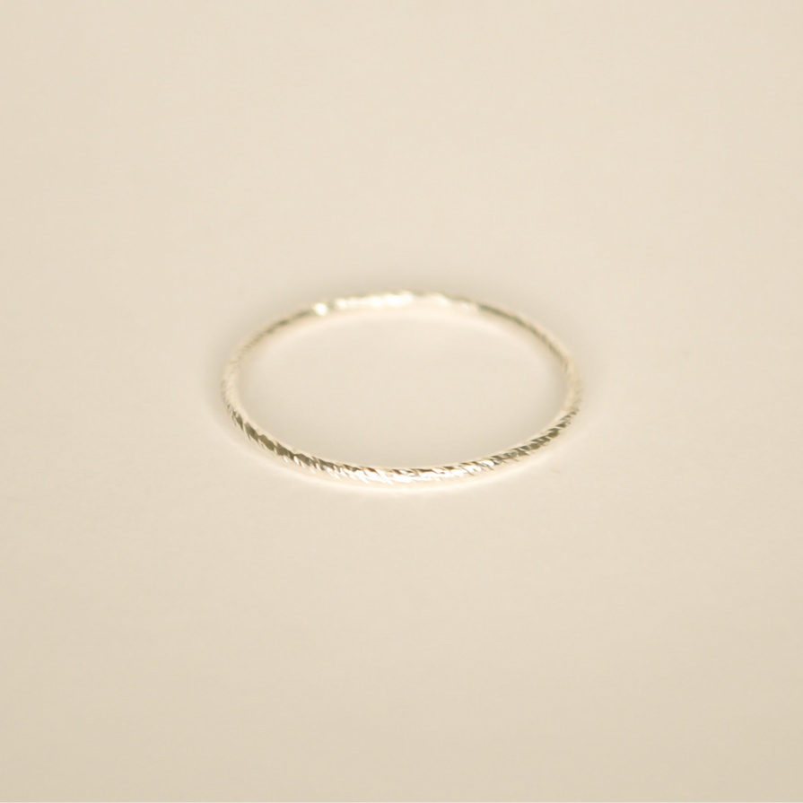 Silver delicate band with subtle texture that catches the light. Pictured on an off white background.
