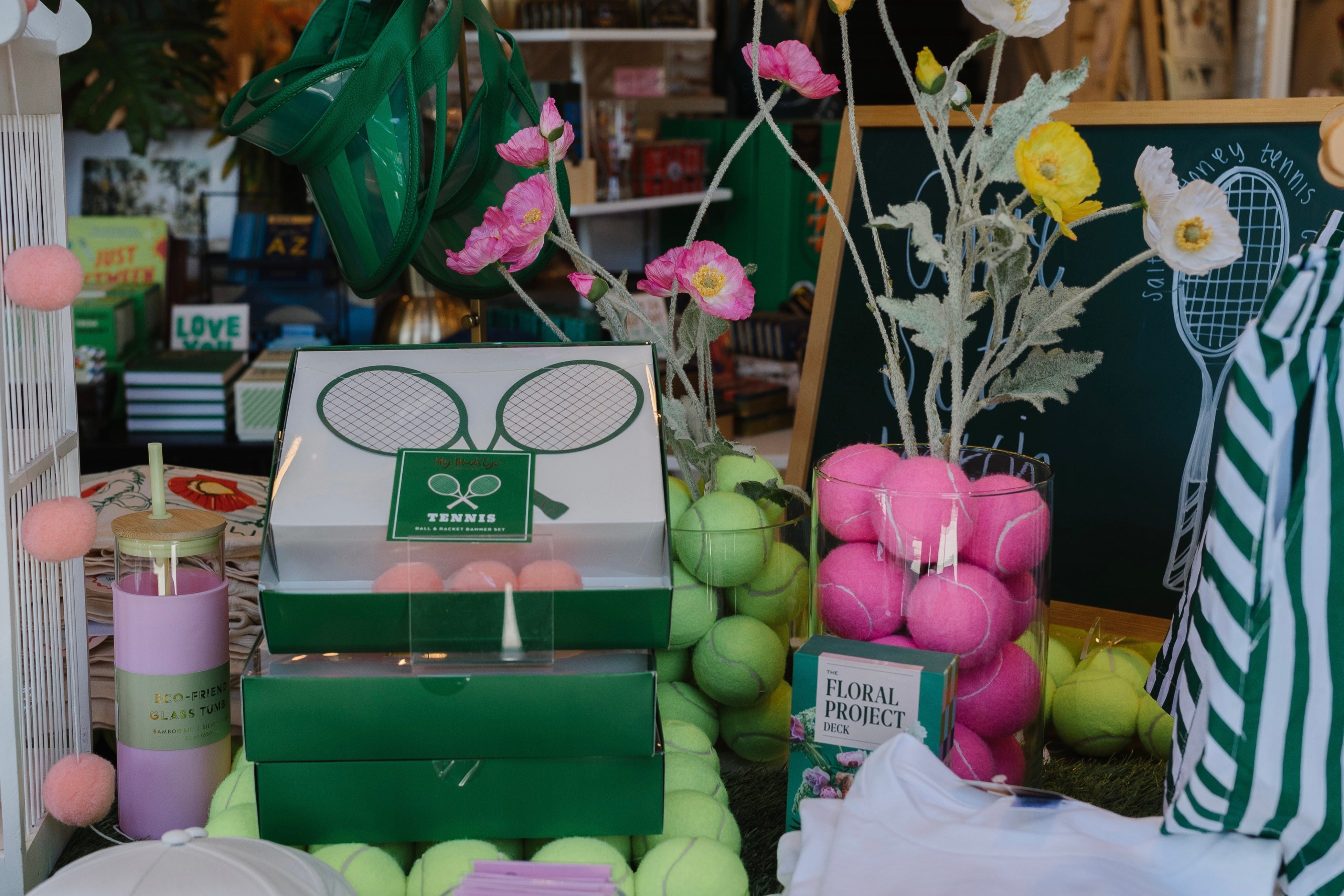 Table with tennis-themed products including candles, towels, and hats in a store setting.