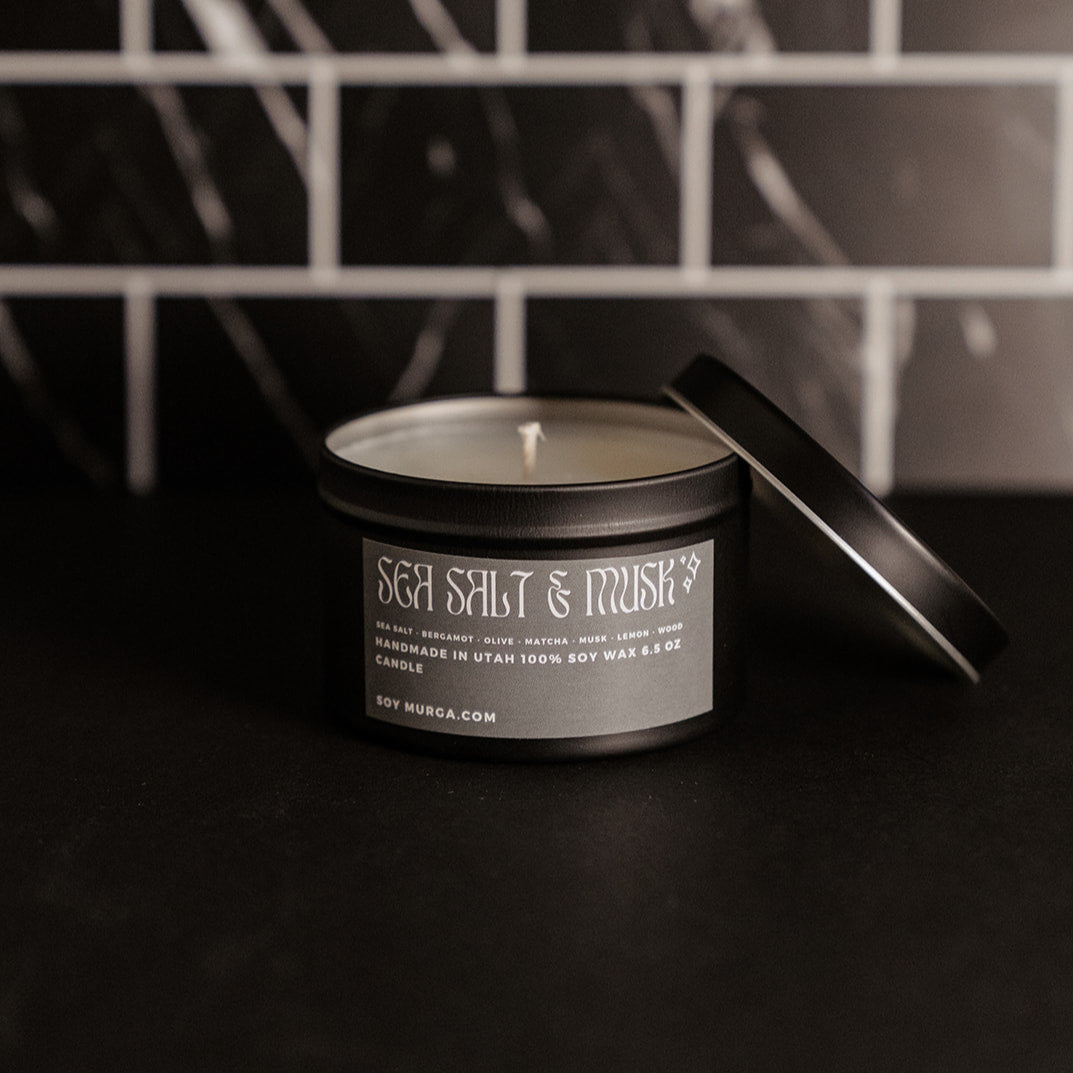 Small black matte candle with a sage green label. Pictured against a black marble back splash.