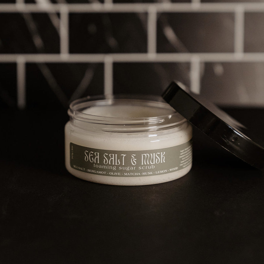 Small clear container with a black lid and sage green label. Pictured against a black marble back splash.