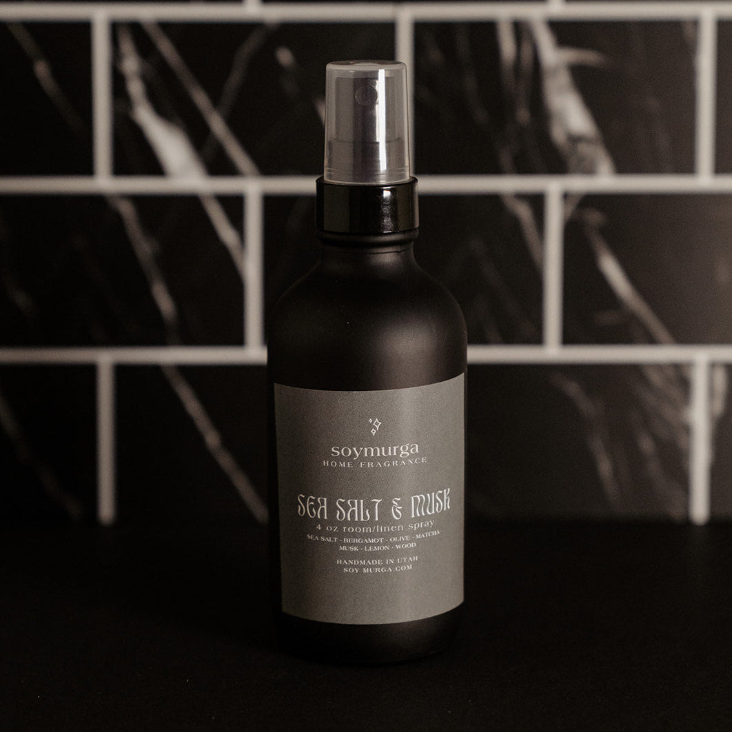 black matte room spray bottle with a sage green label. Pictured against a black marble backsplash. 