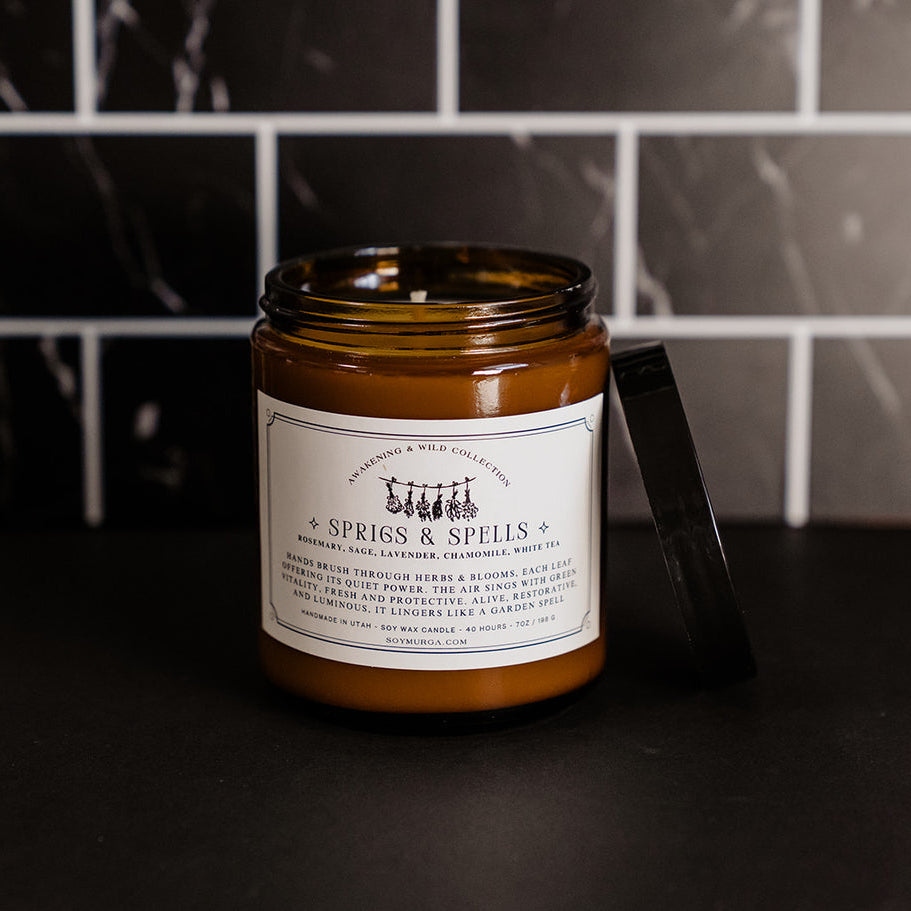 The candle in an amber glass on a black countertop with black marble subway tile in the backgroun. 