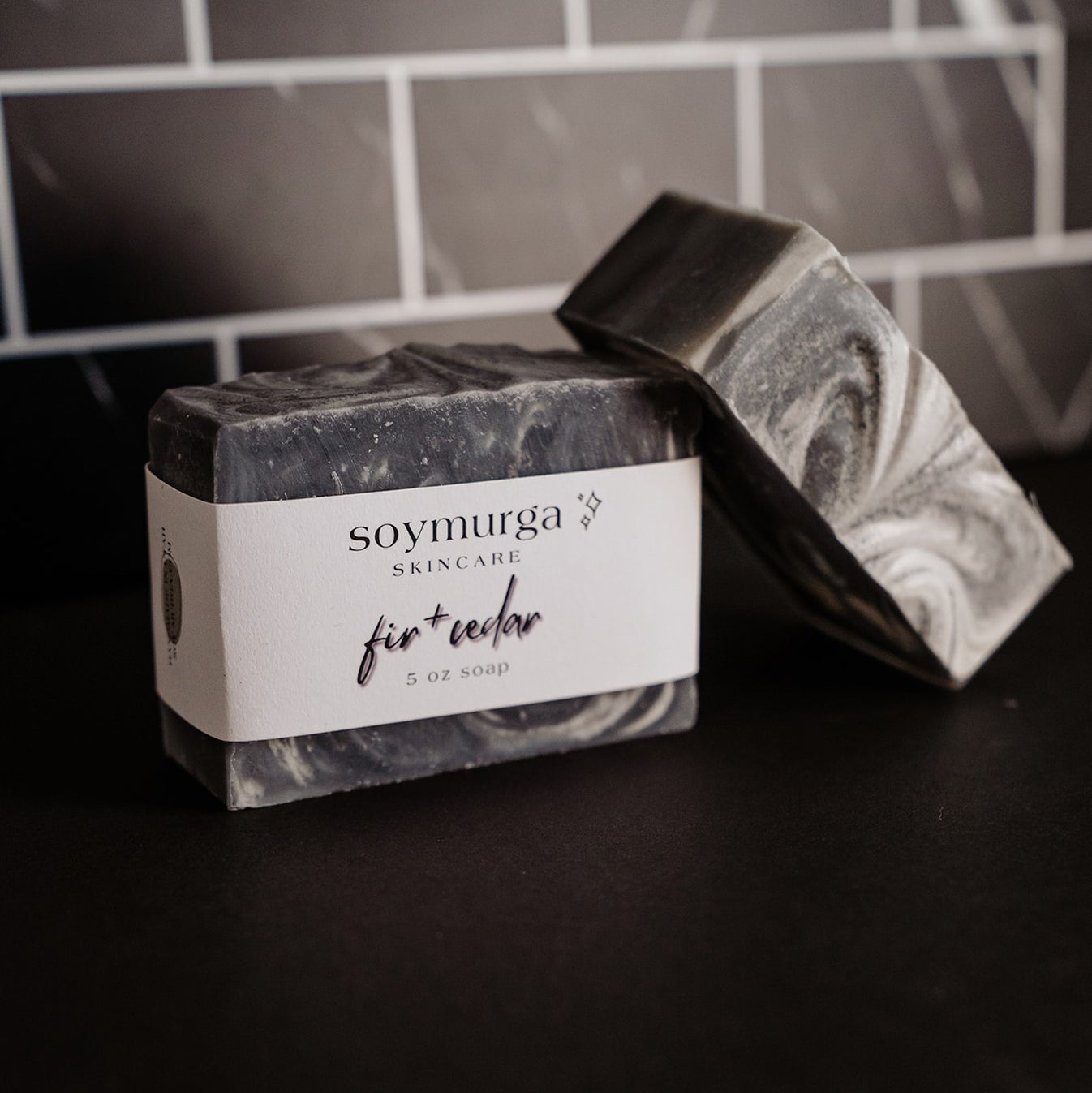 Fir + cedar soap bar on a black countertop with black marble subway tile in the background. 