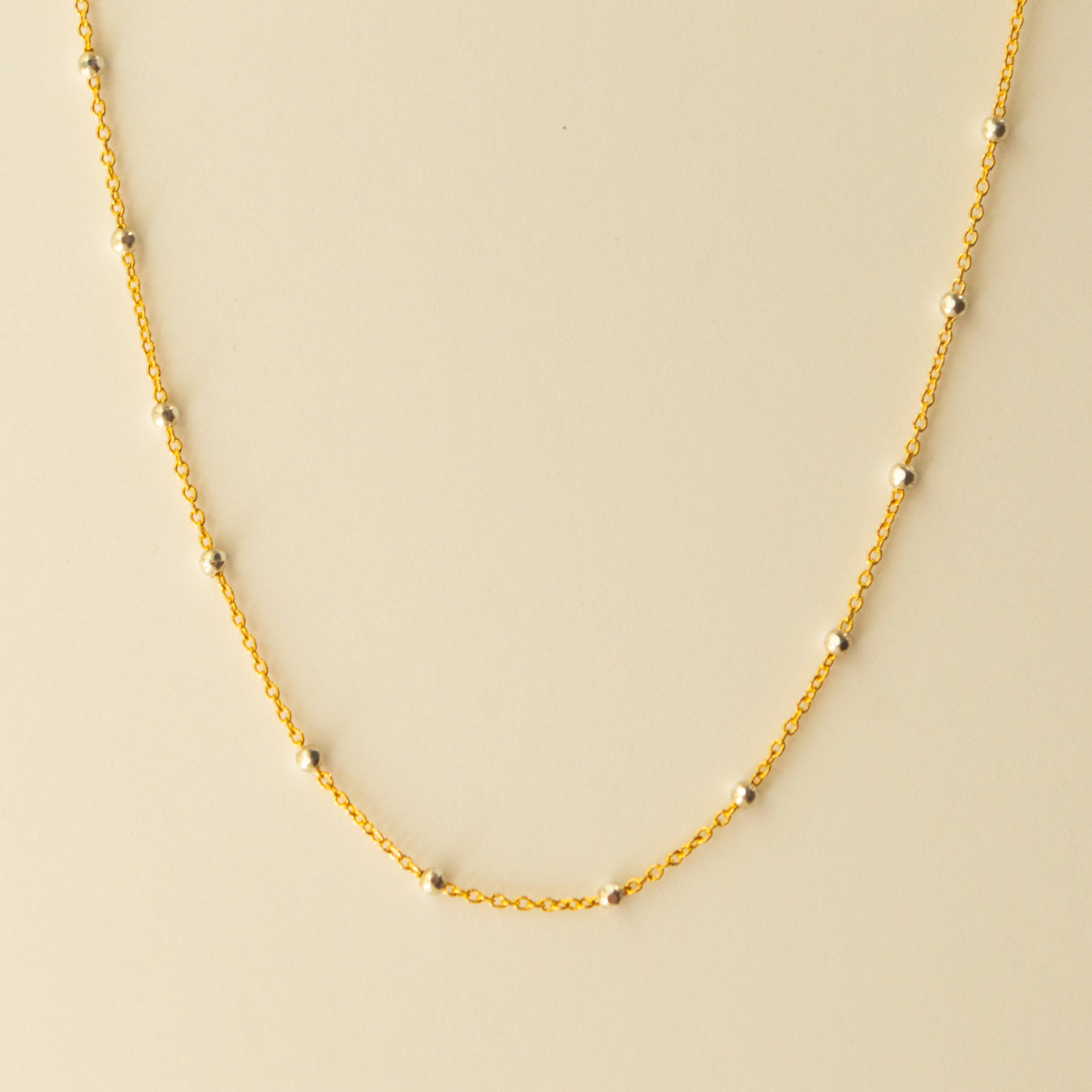 Delicate gold chain with tiny silver beads dotting the length intermittently. Pictured on an off white background.