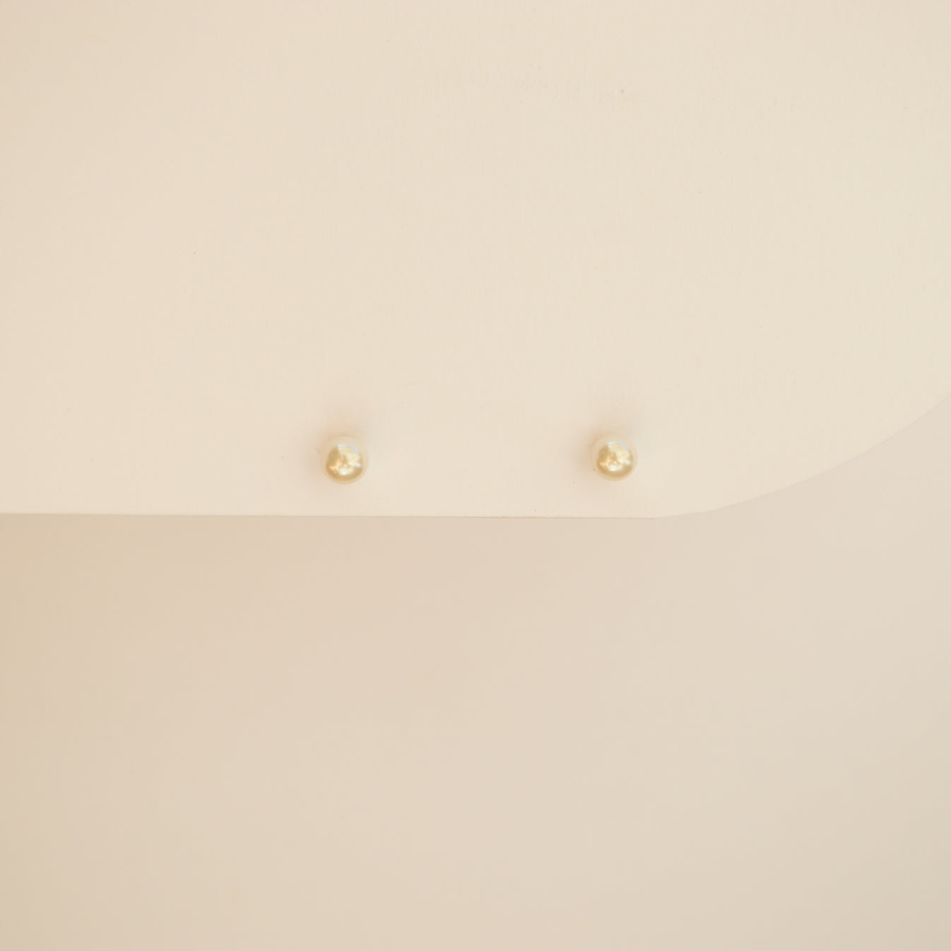 Delicate round pearl studs on a off white background.