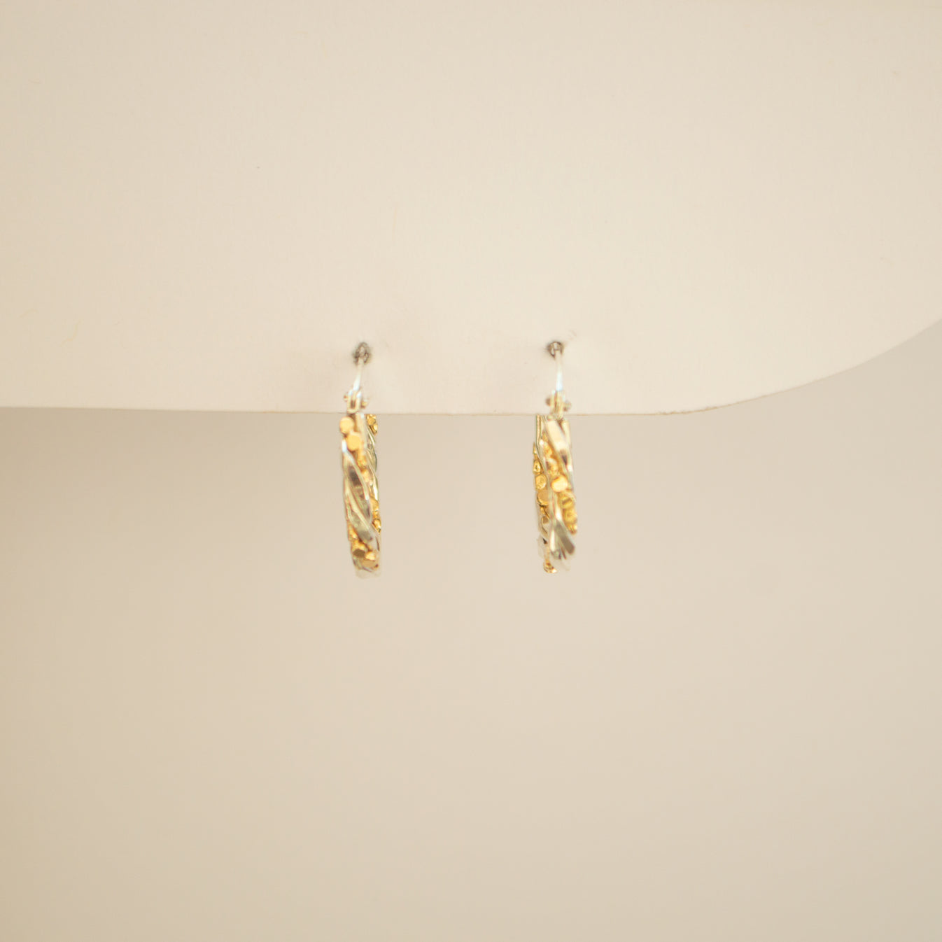 Hoops made from gold and silver twisted together, on an off white background. 