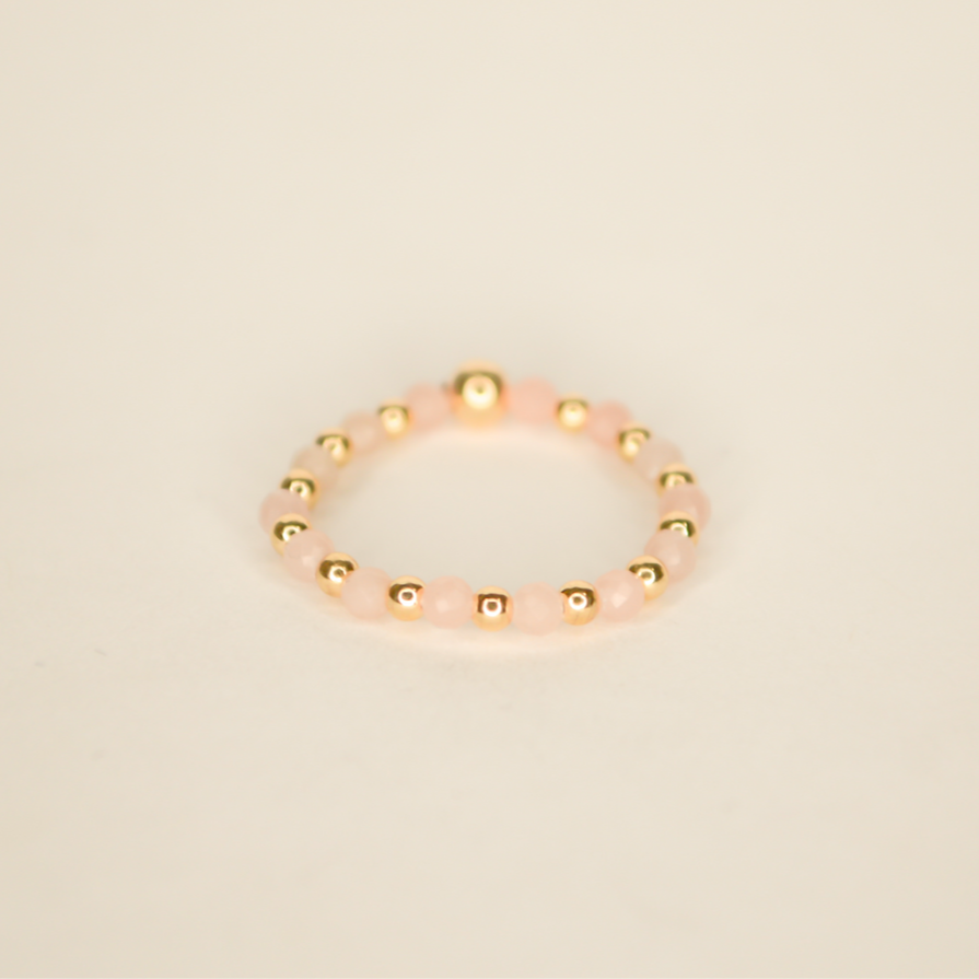 Streatchable beaded ring with pink rose quartz beads alternating with gold beads. Pictured on an off white back ground.