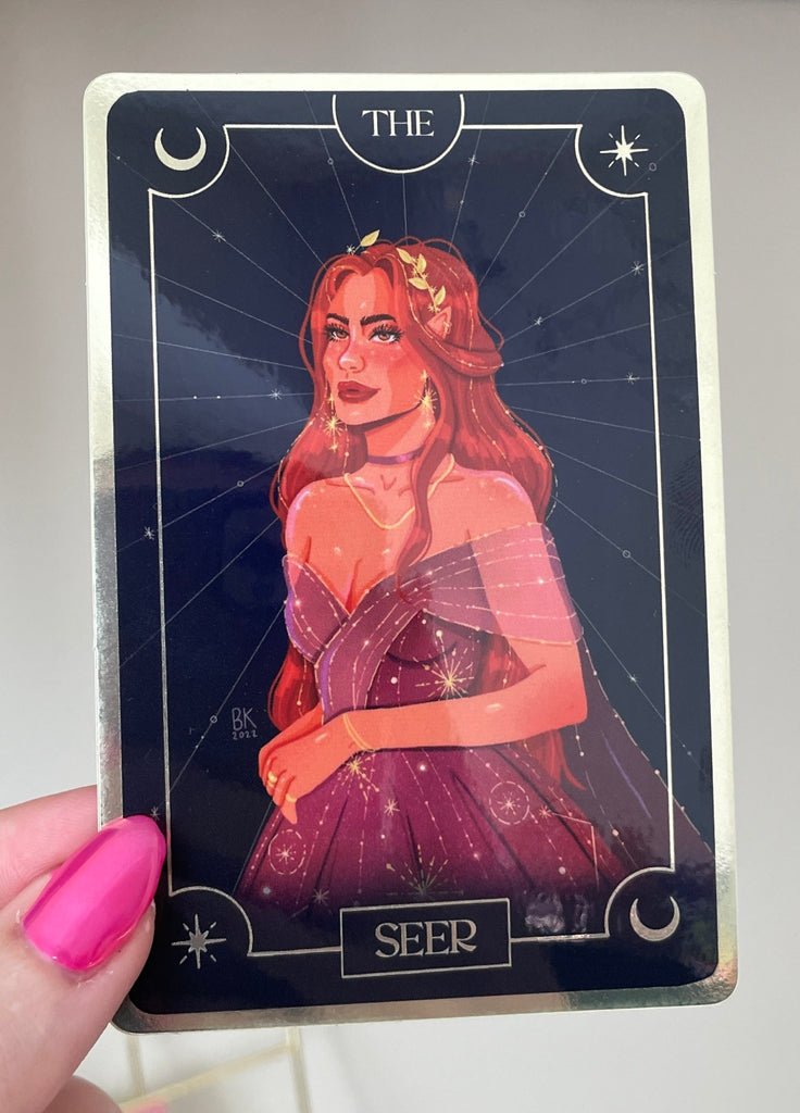 The Seer. A tarot card with a crescent moon and stars in opposing corners. She is wearing a sparkly, purple dress with sleeves that are off the shoulders. She has long, wavy red hair with greenery making a crown on her head. 