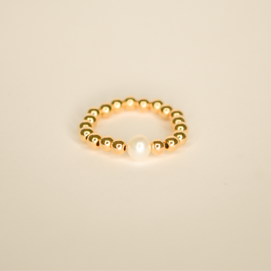 Gold beaded ring with a single large pearl bead. Pictured on an off white back ground.