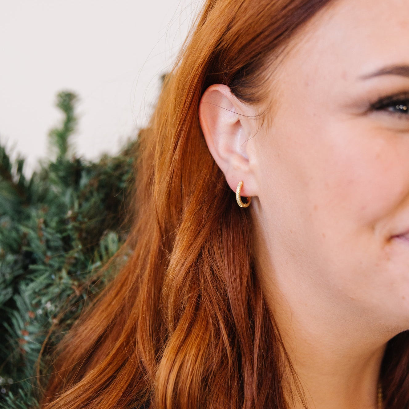 Gold diamond huggie in woman's ear. 