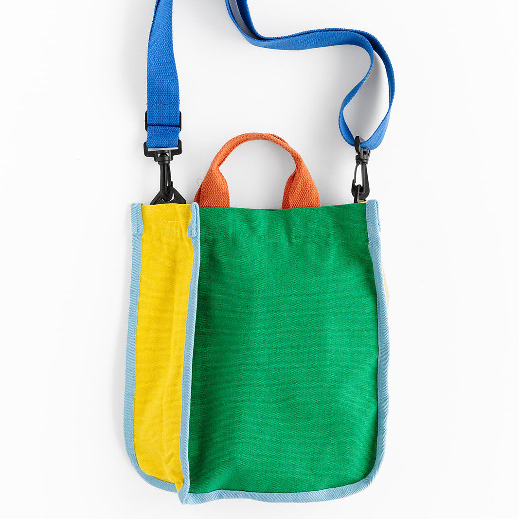 A colorful green and yellow tote bag with light blue trim is shown against a white background, featuring orange handles and a blue adjustable shoulder strap. The bag has black clip hardware connecting the shoulder strap to the sides. 