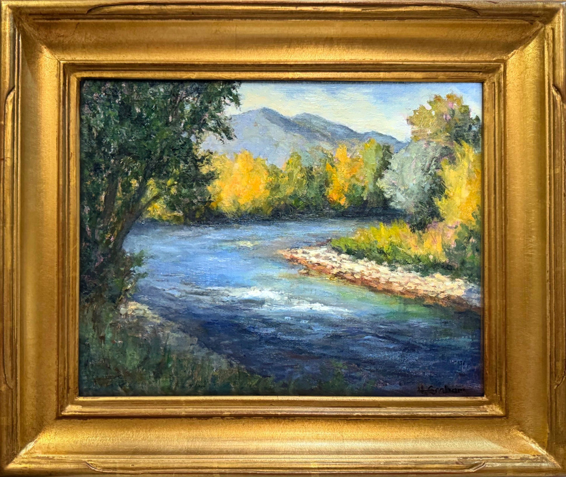 A view of a river bending to the right with golden green trees lining the water. 