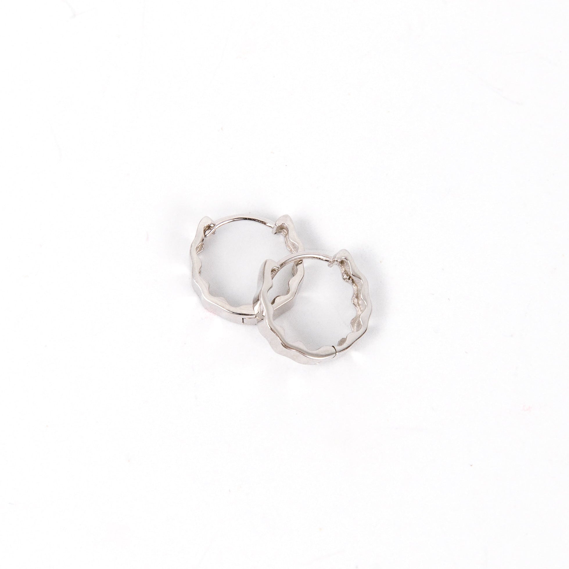 Two small silver hoop earrings with wavy edges, displayed upright on a white background