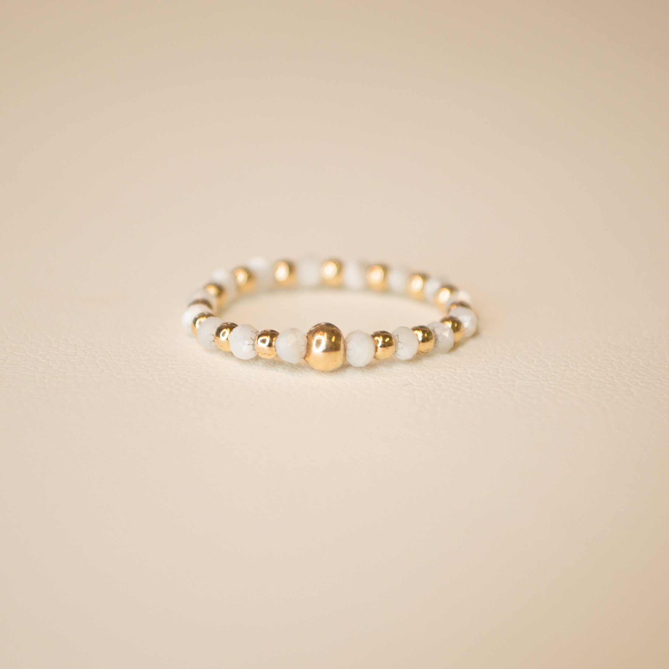 Stretchable beaded ring with mother of pearl beads alternating with gold beads. Pictured on an off white back ground.