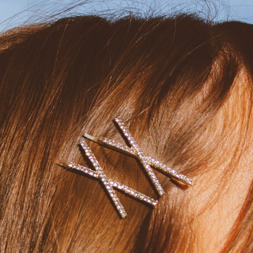 Add some sparkle to your hair with this 2-pack of crystal crossed bobby pins. The gold metal adds an elegant touch while the crystals add just the right amount of bling. Secure your hair with style!