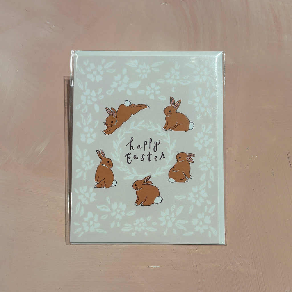 light pink card with a white floral design and five bunnies reading "Happy Easter"
