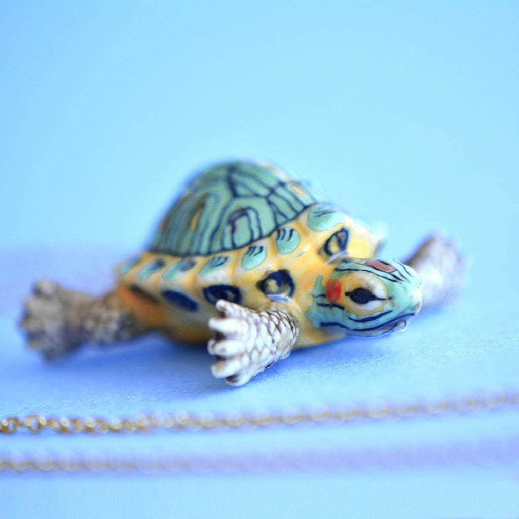 Experience the joy of turtle companionship—no feeding required—with our limited-edition Turtle Necklace! This handcrafted porcelain pendant captures the charm of the red-eared slider, America's most beloved pet turtle, in exquisite detail. Strung on a delicate chain, this necklace is a versatile and endearing addition to any ensemble, from casual daywear to elegant evening attire.