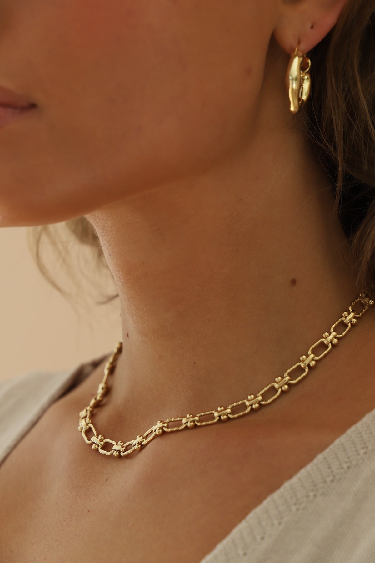 Close-up of a person wearing a gold chain necklace and hoop earrings.