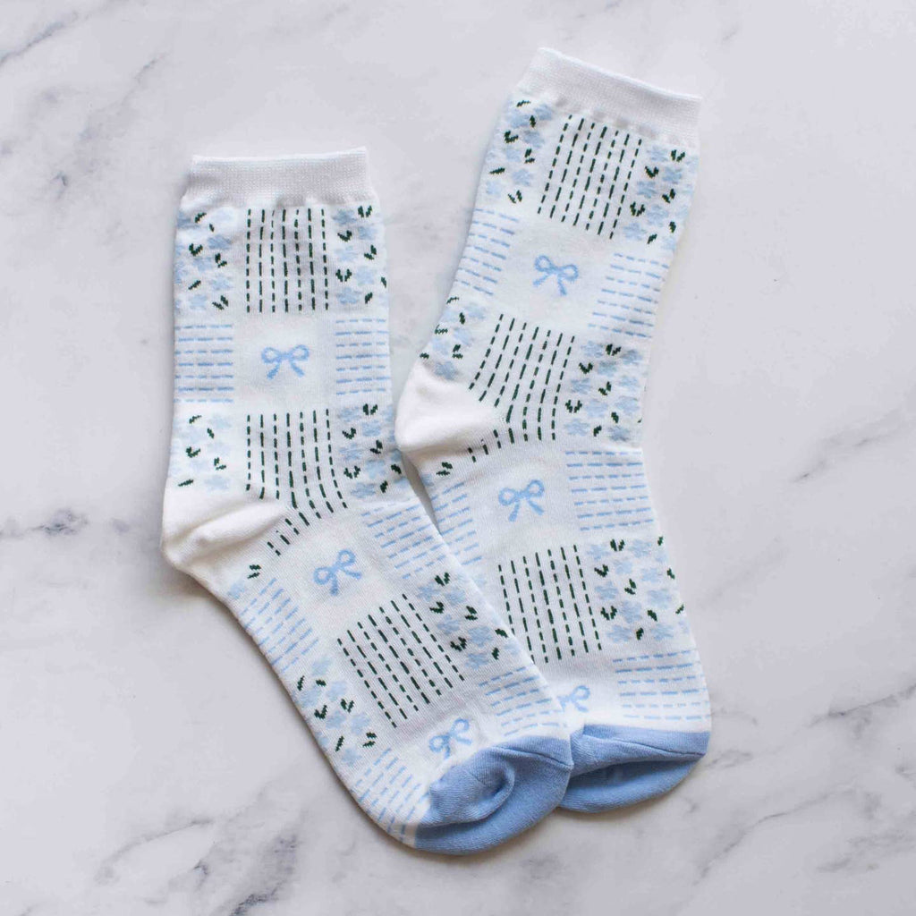 Slip into style with our Blue Remi Ribbon & Floral Socks. The light blue floral pattern and delicate tiny bows add a touch of elegance to these crew socks. Step up your sock game and treat your feet while showing off your fashion sense.