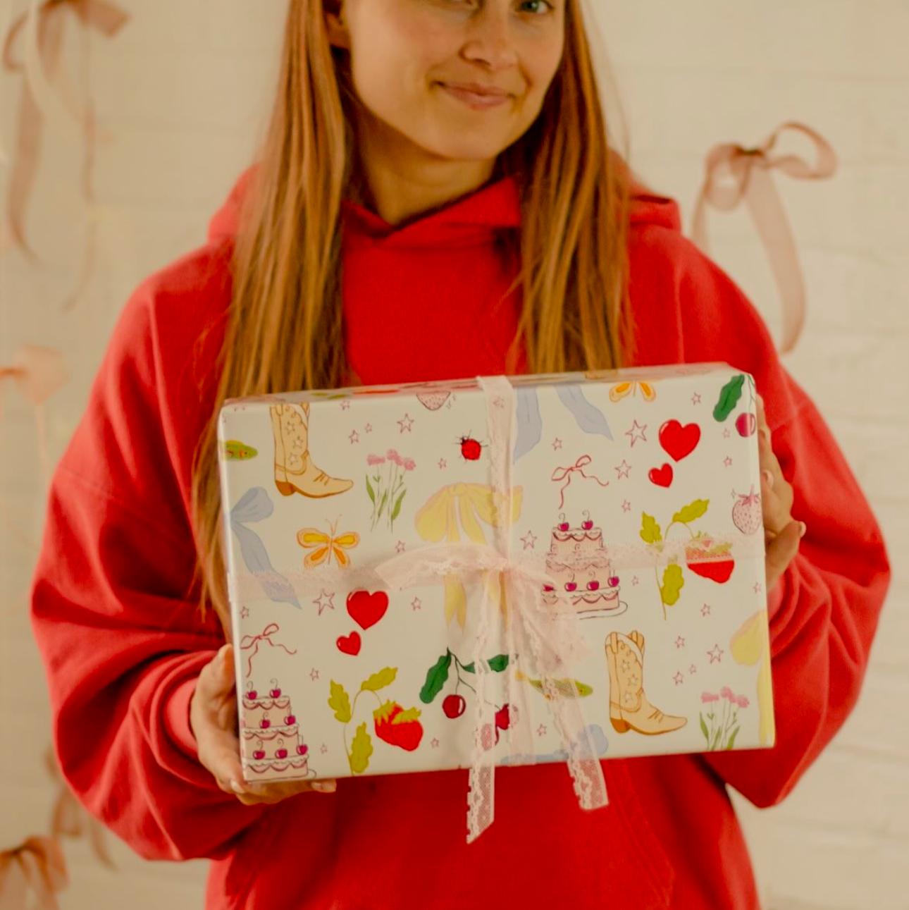 cream colored wrapping paper with an assortment of different objects - hearts, stars, cowboy boots, flowers, cakes, and strawberries