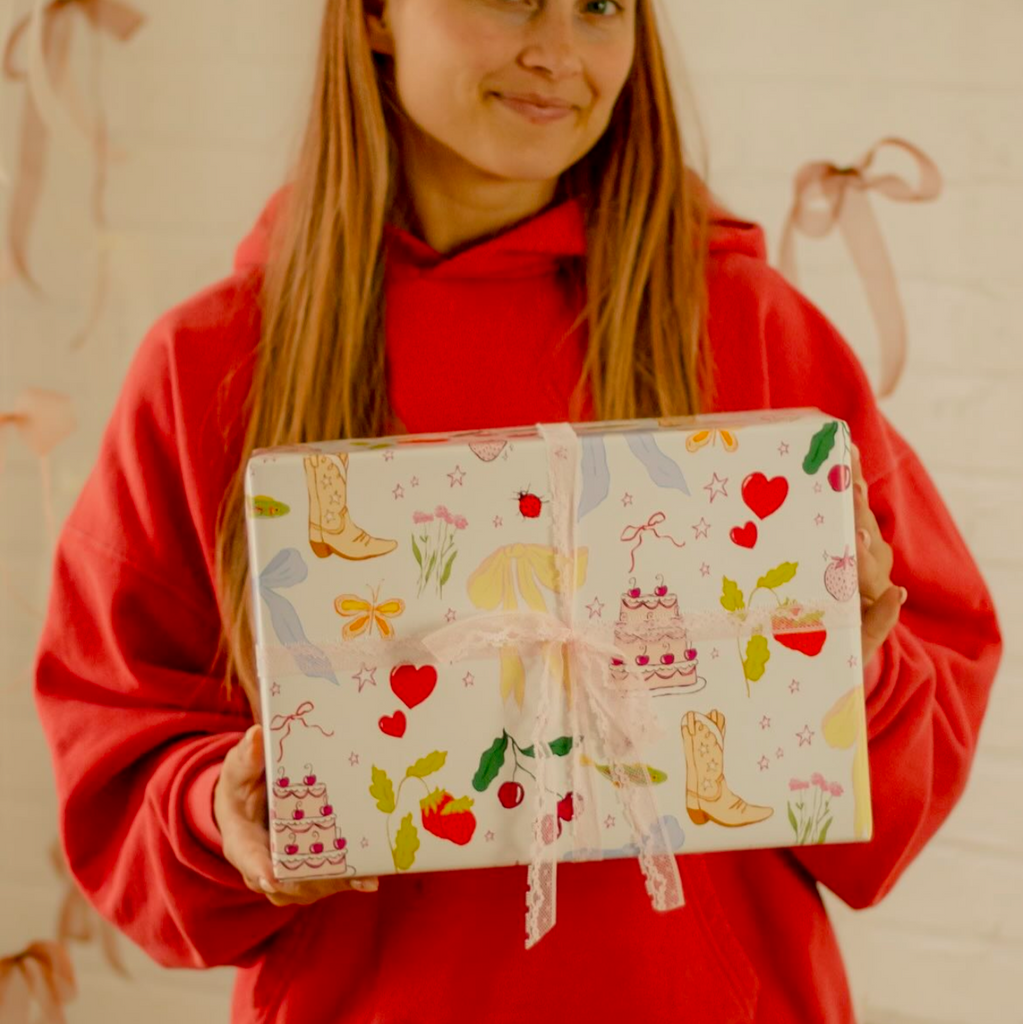 cream colored wrapping paper with an assortment of different objects - hearts, stars, cowboy boots, flowers, cakes, and strawberries