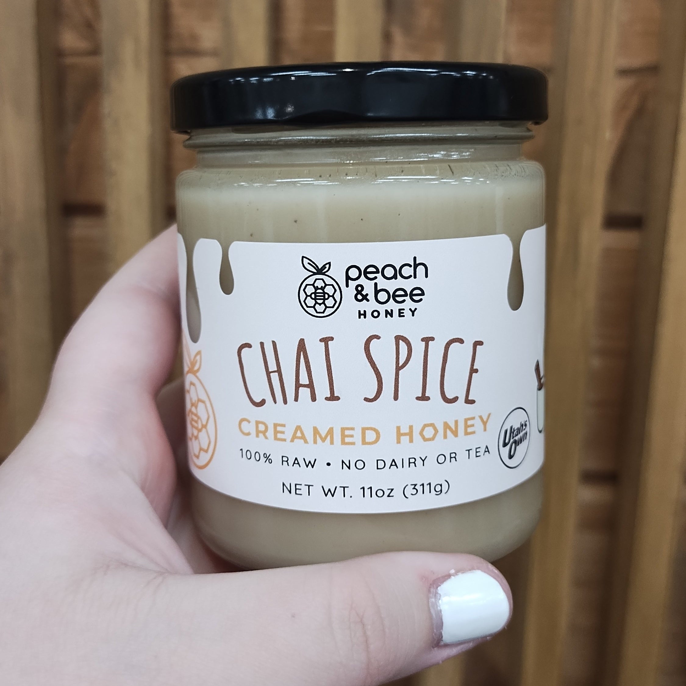 Hand holding a jar of 'Chai Spice' honey with a wooden background