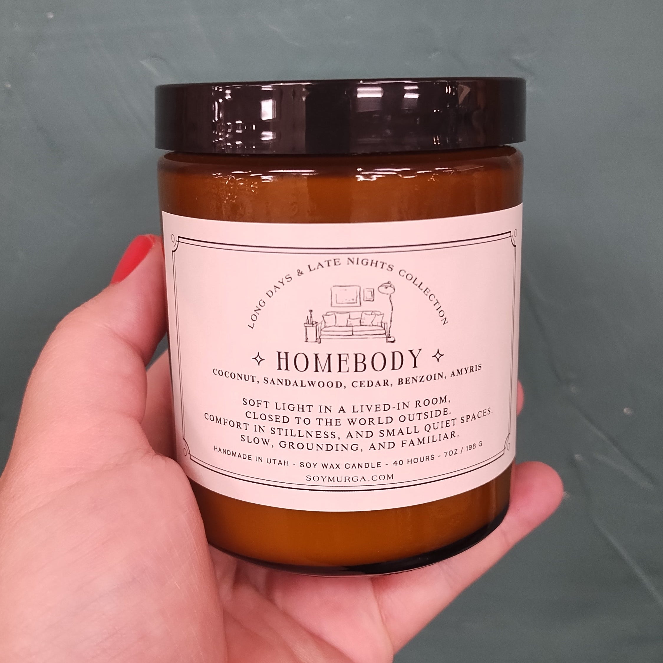 amber jar with black lid and cream label. Held in woman's hand against a teal backdrop.