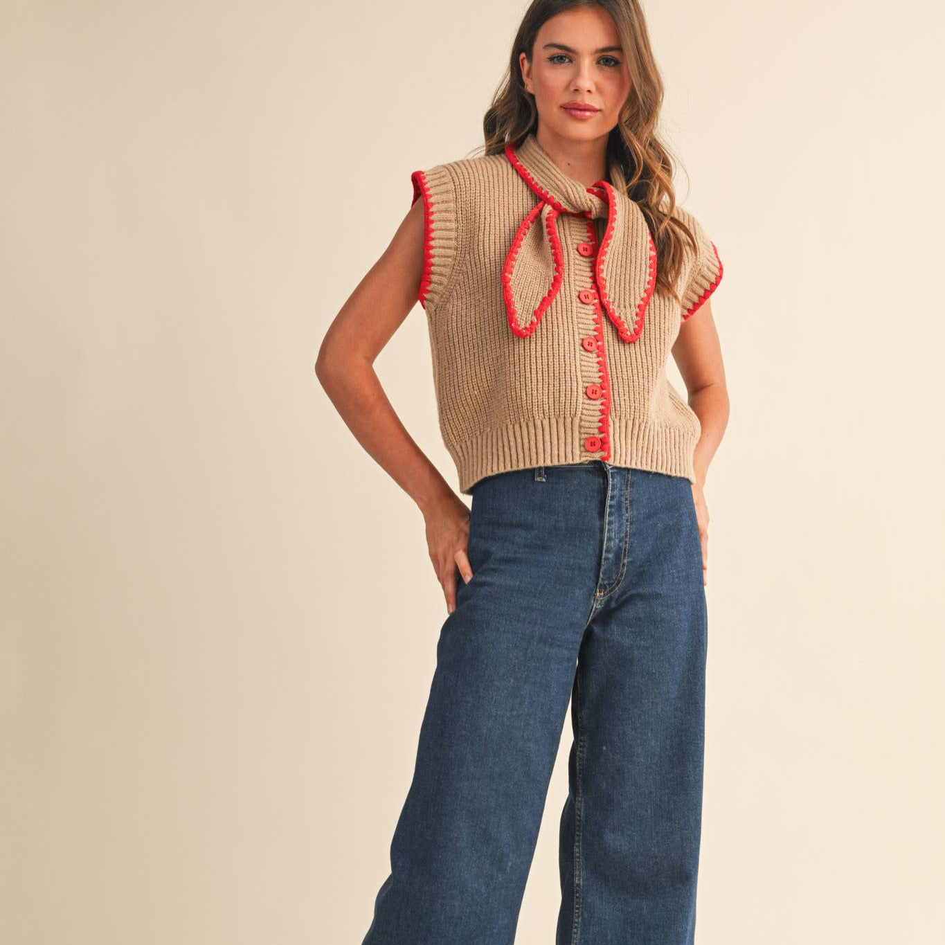 This cozy knit sweater vest features a mocha bodice accented with a vibrant red neck tie and matching red edging with a contrast blanket stitch. Designed for layering, it offers warmth and style, making it perfect for adding a touch of classic charm to any outfit. Comfortable and versatile, it’s an ideal choice for cooler days.