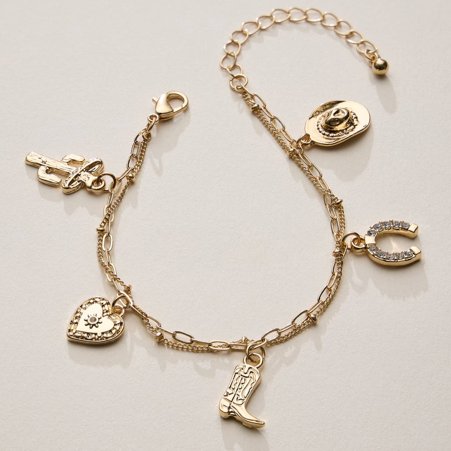 Embrace Western-inspired style with this trendy gold charm bracelet, featuring double-layered chain links and a collection of cowgirl-inspired charms. Designed with detailed pendants, including a cowboy boot, cowboy hat, horseshoe, cactus, and a sparkling heart charm, this bracelet is the perfect accessory for adding a touch of rustic charm to any outfit. Lightweight and adjustable, it’s ideal for everyday wear or special occasions.