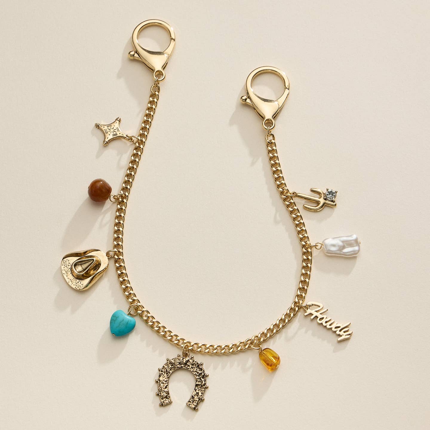 Add a western flair to your handbag with this gold chain bag strap featuring cowboy-inspired charms, including a horseshoe, cowboy hat, cactus, and turquoise heart. A stylish and unique accessory.