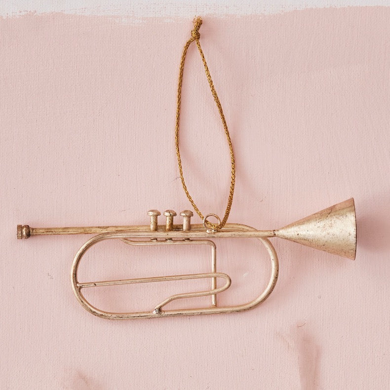 Gold trumpet ornament hanging on a pink background