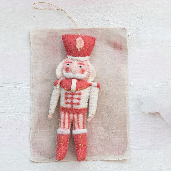 Felted nutcracker ornament on a textured beige background
