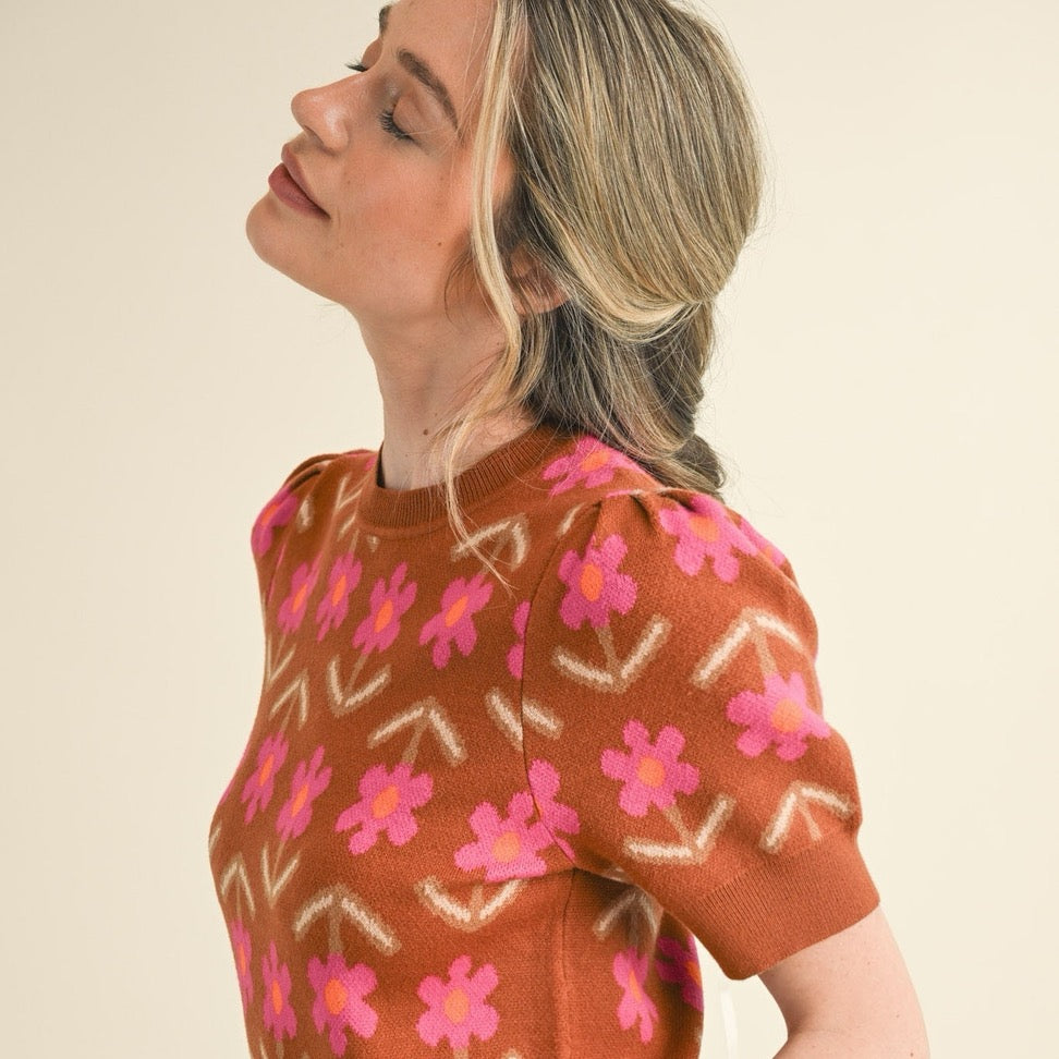 Embrace effortless style with this charming short sleeve knit sweater in warm mocha tones. Delicate pink flowers dance across the fabric, adding a touch of natural beauty to your everyday wardrobe. The soft, breathable knit construction keeps you comfortable whether you're layering for cooler days or wearing it solo when temperatures rise. Perfect for transitional seasons, this versatile piece pairs beautifully with jeans, skirts, or trousers for a look that feels both polished and approachable.