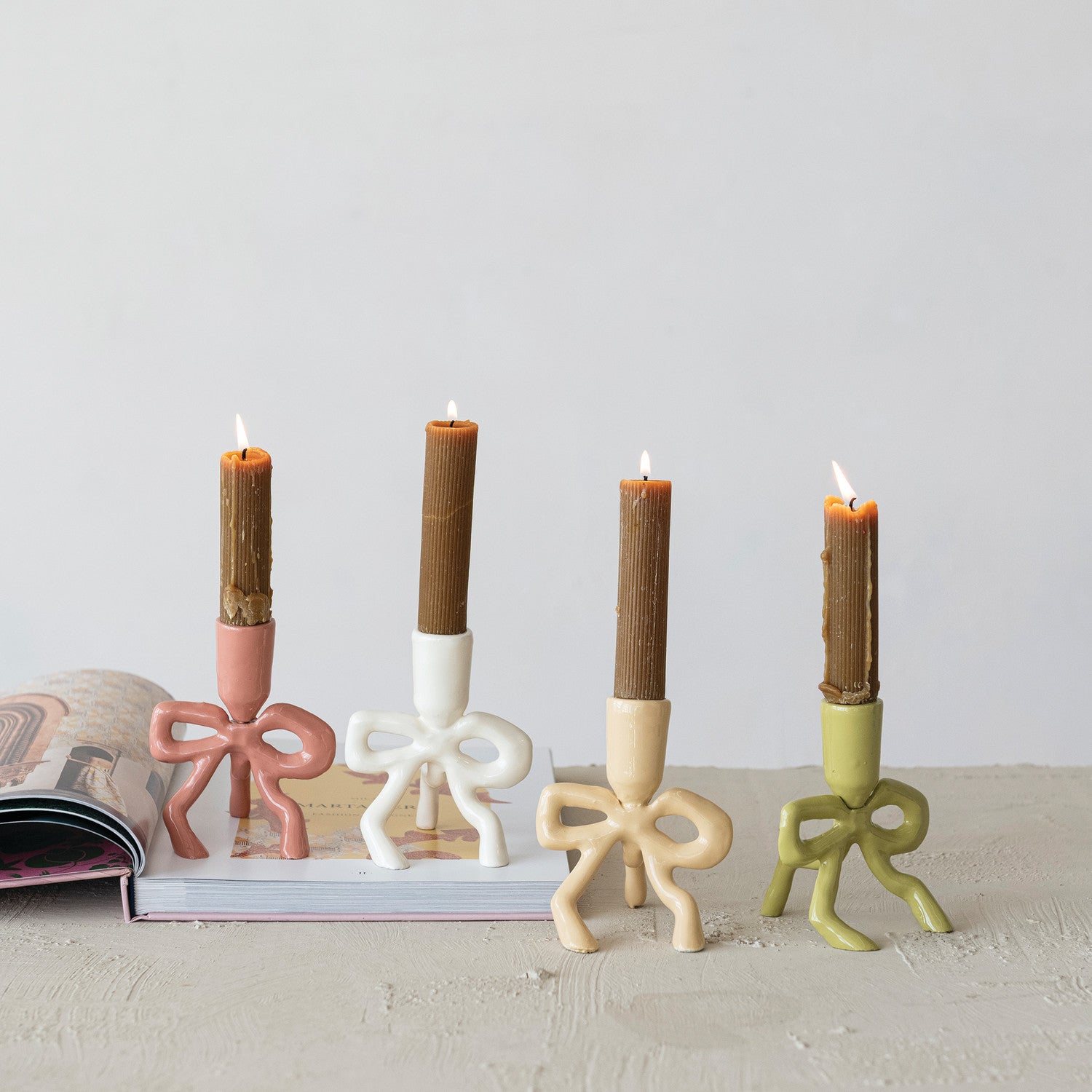 Add a touch of whimsy and elegance to your space with this Enameled Cast Aluminum Taper Holder. Featuring a charming bow-shaped base, this candlestick holder is perfect for adding ambient lighting to any room. Available in 4 delightful color options to match your decor.