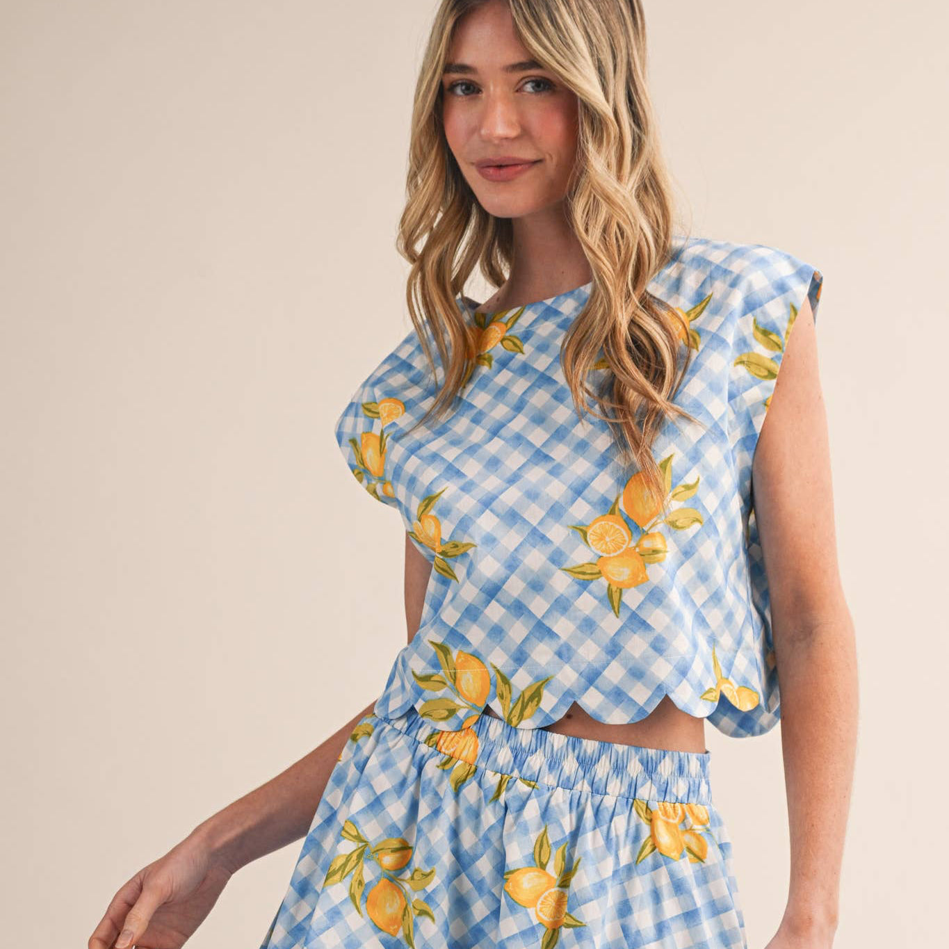 Brighten your wardrobe with this charming gingham top that brings effortless style to every season. The cheerful lemon-inspired print and delicate scalloped hem create a look that feels both playful and polished. Designed with a semi-cropped silhouette, round neckline, and sweet cap sleeves, it's the perfect piece for layering or wearing solo. The keyhole back with button closure adds a thoughtful touch of detail, while 100% cotton keeps you comfortable all day long.