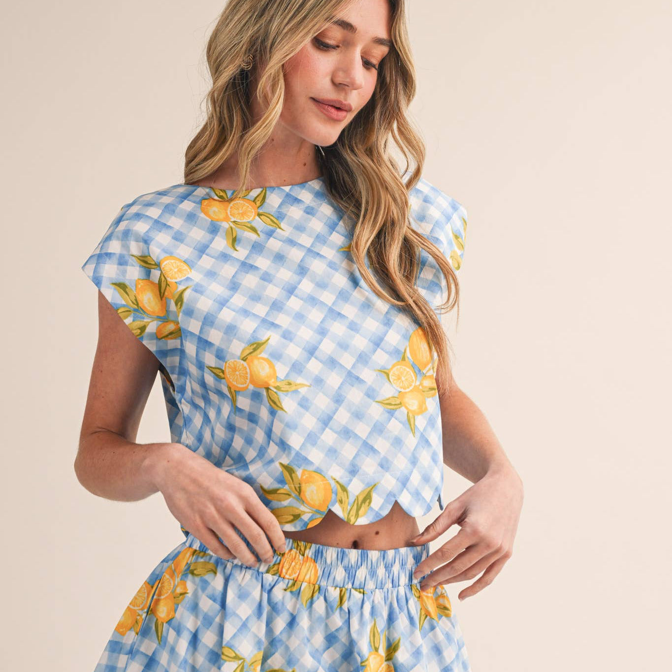 Brighten your wardrobe with this charming gingham top that brings effortless style to every season. The cheerful lemon-inspired print and delicate scalloped hem create a look that feels both playful and polished. Designed with a semi-cropped silhouette, round neckline, and sweet cap sleeves, it's the perfect piece for layering or wearing solo. The keyhole back with button closure adds a thoughtful touch of detail, while 100% cotton keeps you comfortable all day long.