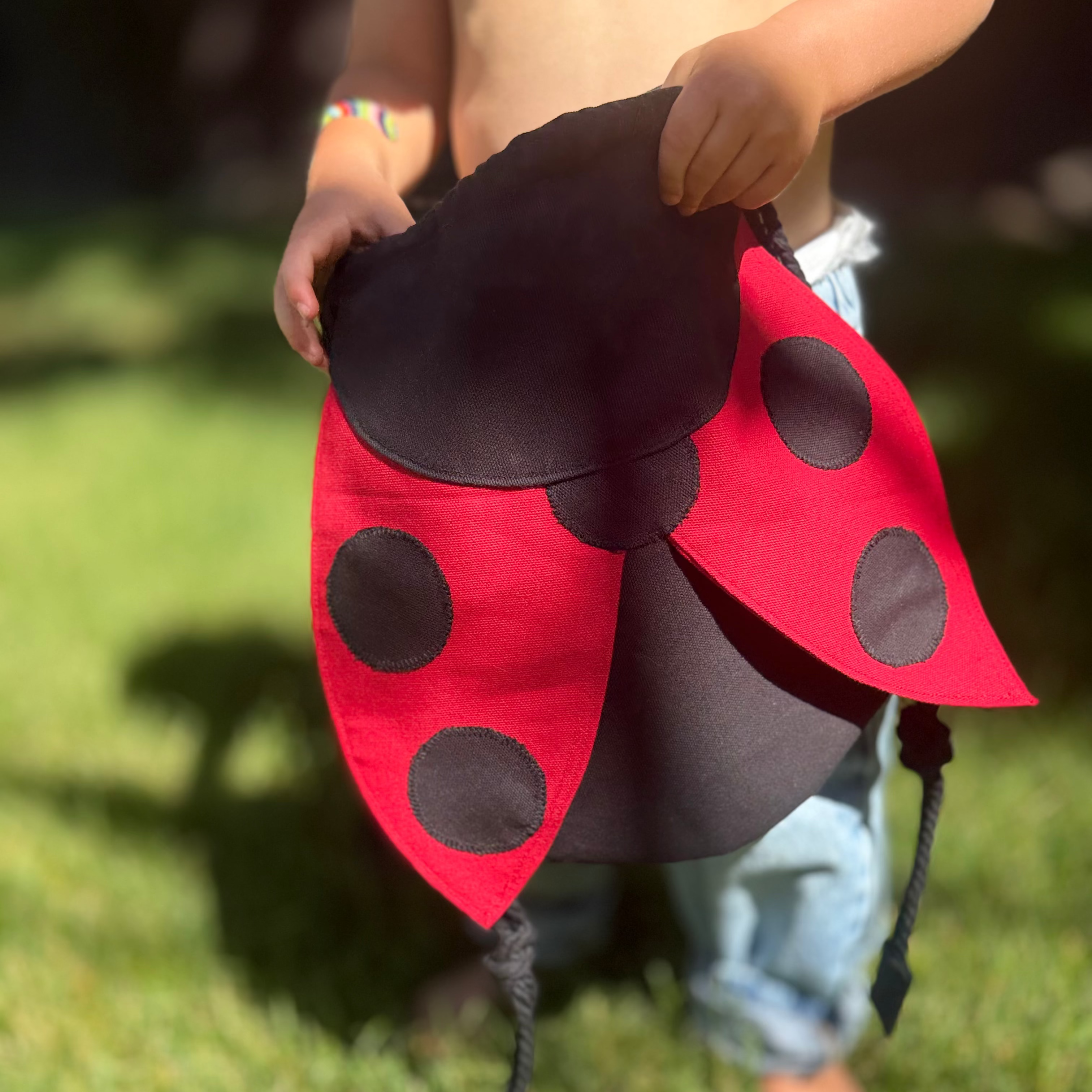 Small children's drawstring backpack with red ladybug wing flaps. 