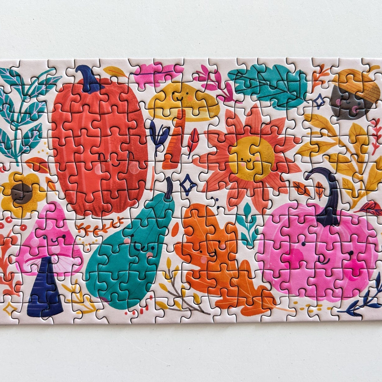 Mini Happy Fall puzzle, design includes brightly colored pumpkins, leaves, flowers, mushrooms, and acorns. Pictured on a white background.