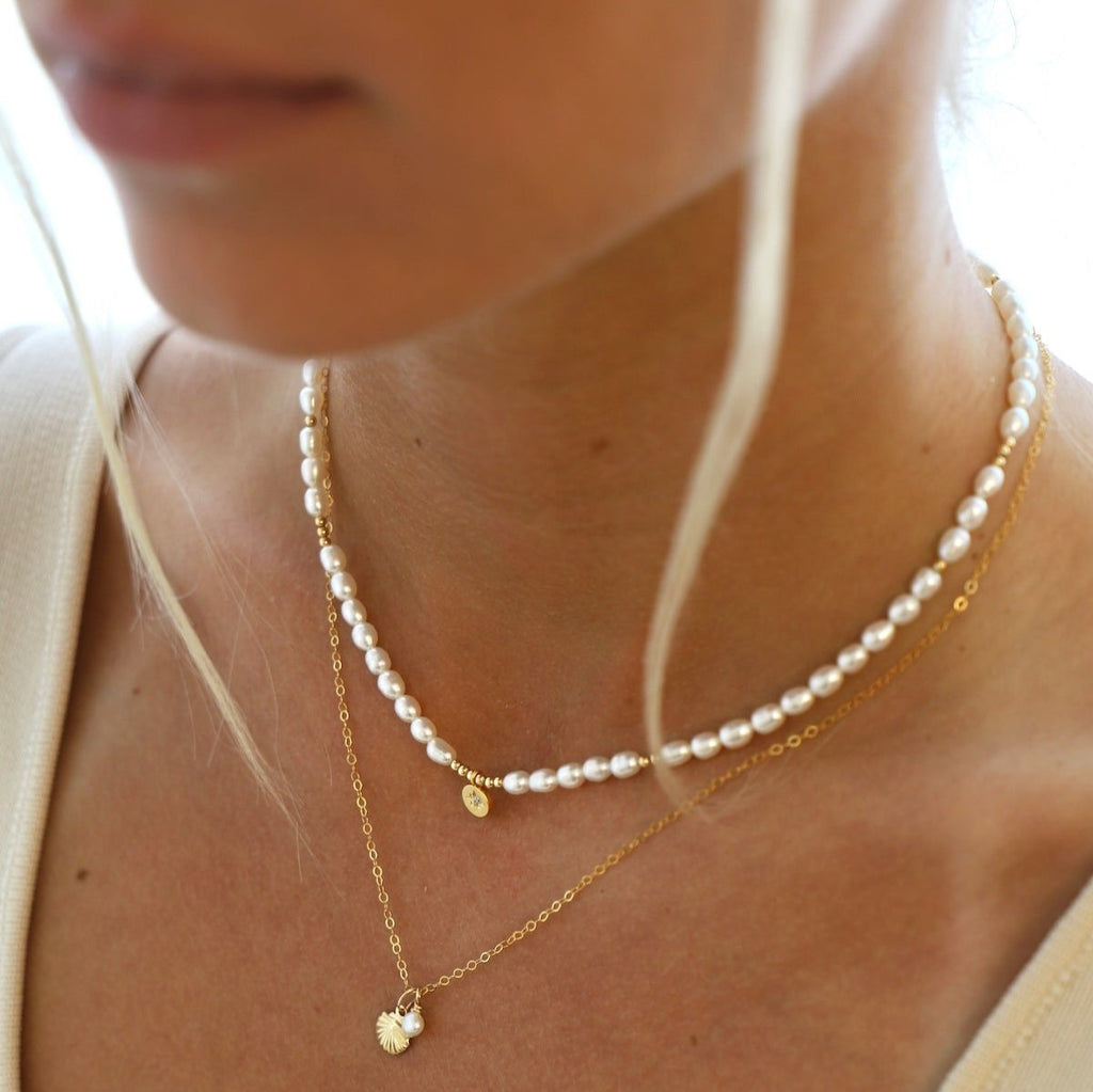 The Kai Necklace. A golden seashell necklace adorned with a pearl. It's an eye-catching piece that will bring a touch of sea inspired beauty to any look. It's classic simplicity is sure to last you all Summers to come. In gold