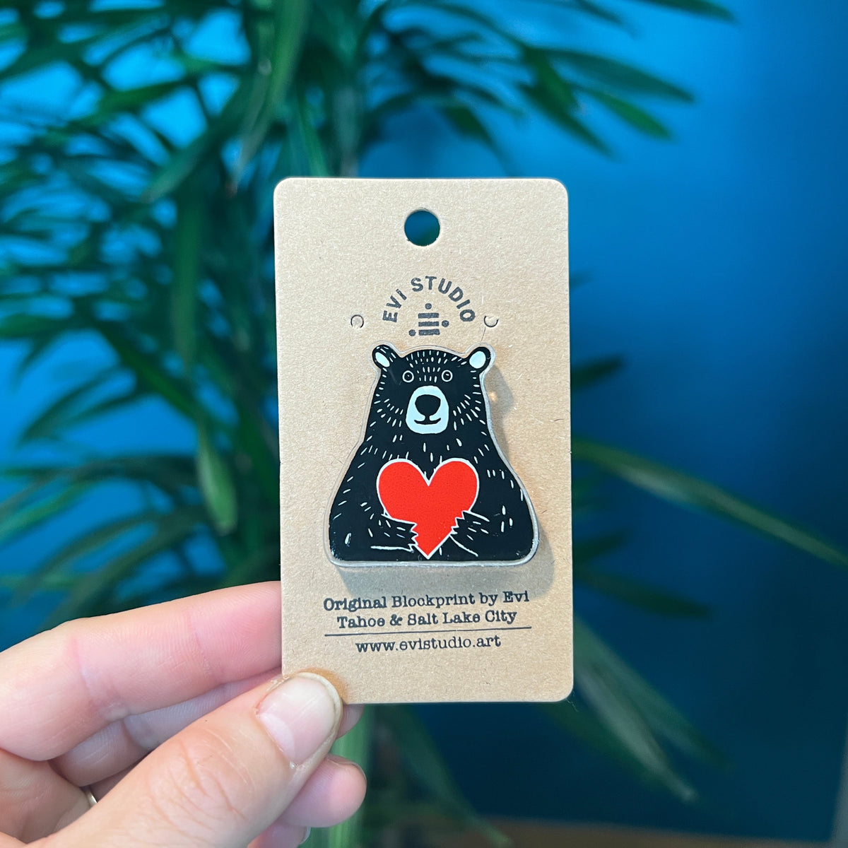 Black bear hugs a bright red heart in this acrylic pin. Held in woman's hand.