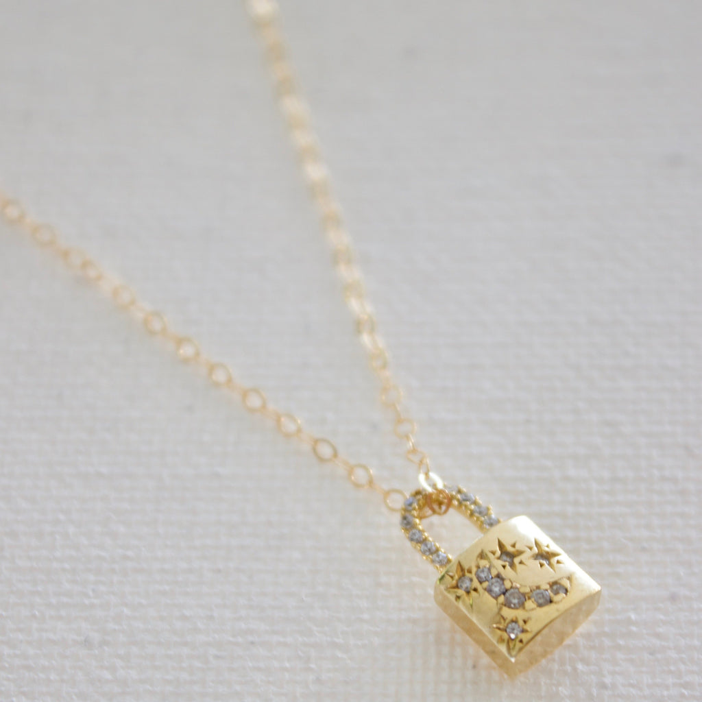 Add a touch of cosmic charm to your look with our Celestial Lock Charm Necklace. Crafted with a petite gold plate lock charm, accented with delicate cz star and moon embellishments. Perfect for adding a subtle, yet eye-catching detail to any outfit. Elevate your style with this enchanting accessory.