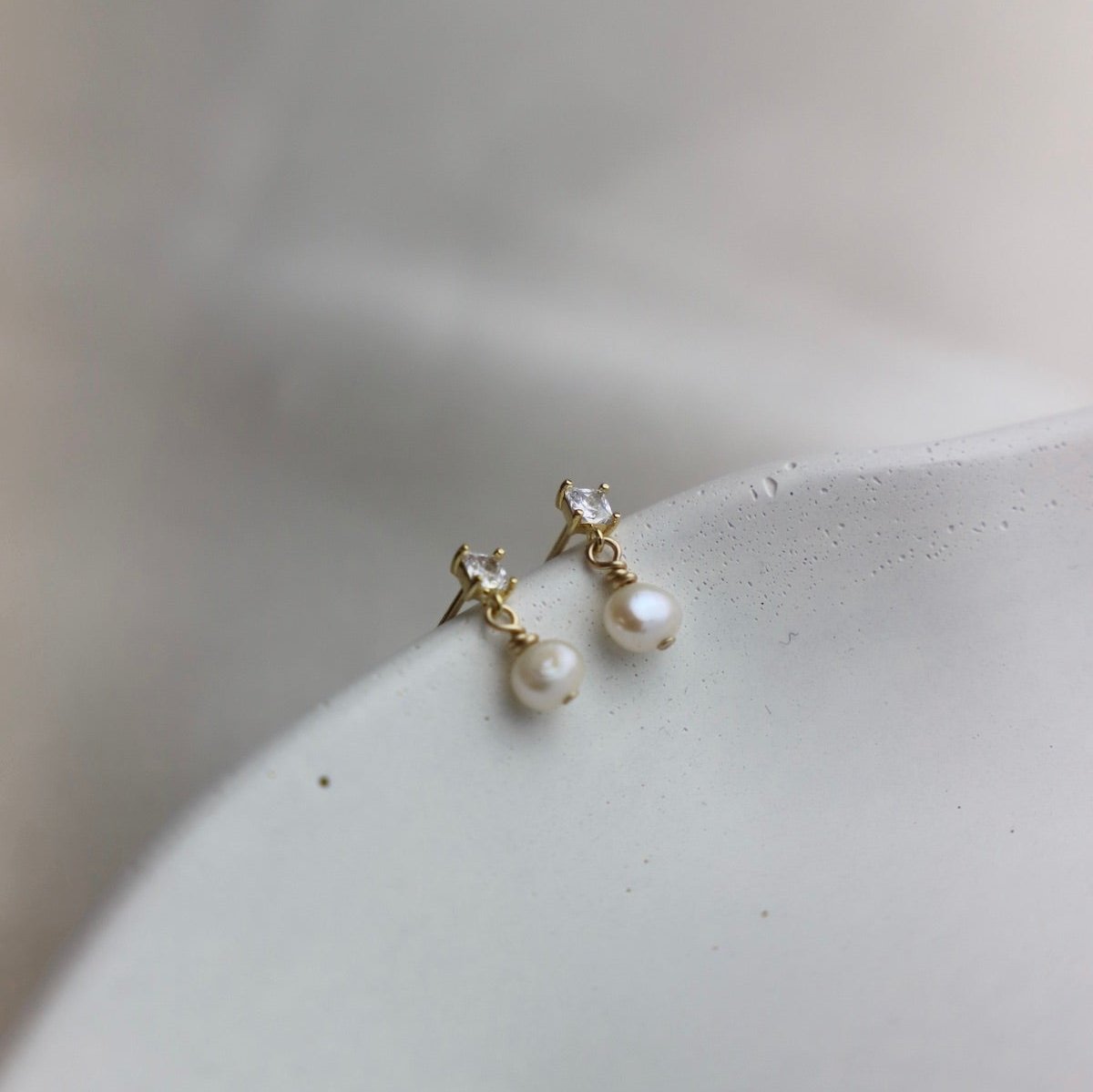 Add a touch of elegance with Claire Pearl Studs. These miniature cz square studs feature a freshwater pearl drop that will elevate any outfit. Perfect for those who love a hint of quirk and sophistication.