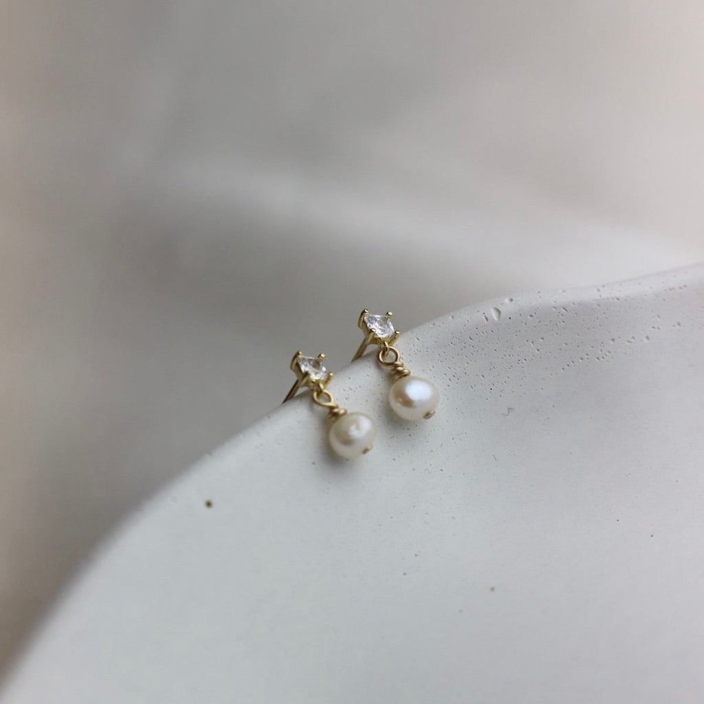 Add a touch of elegance with Claire Pearl Studs. These miniature cz square studs feature a freshwater pearl drop that will elevate any outfit. Perfect for those who love a hint of quirk and sophistication.