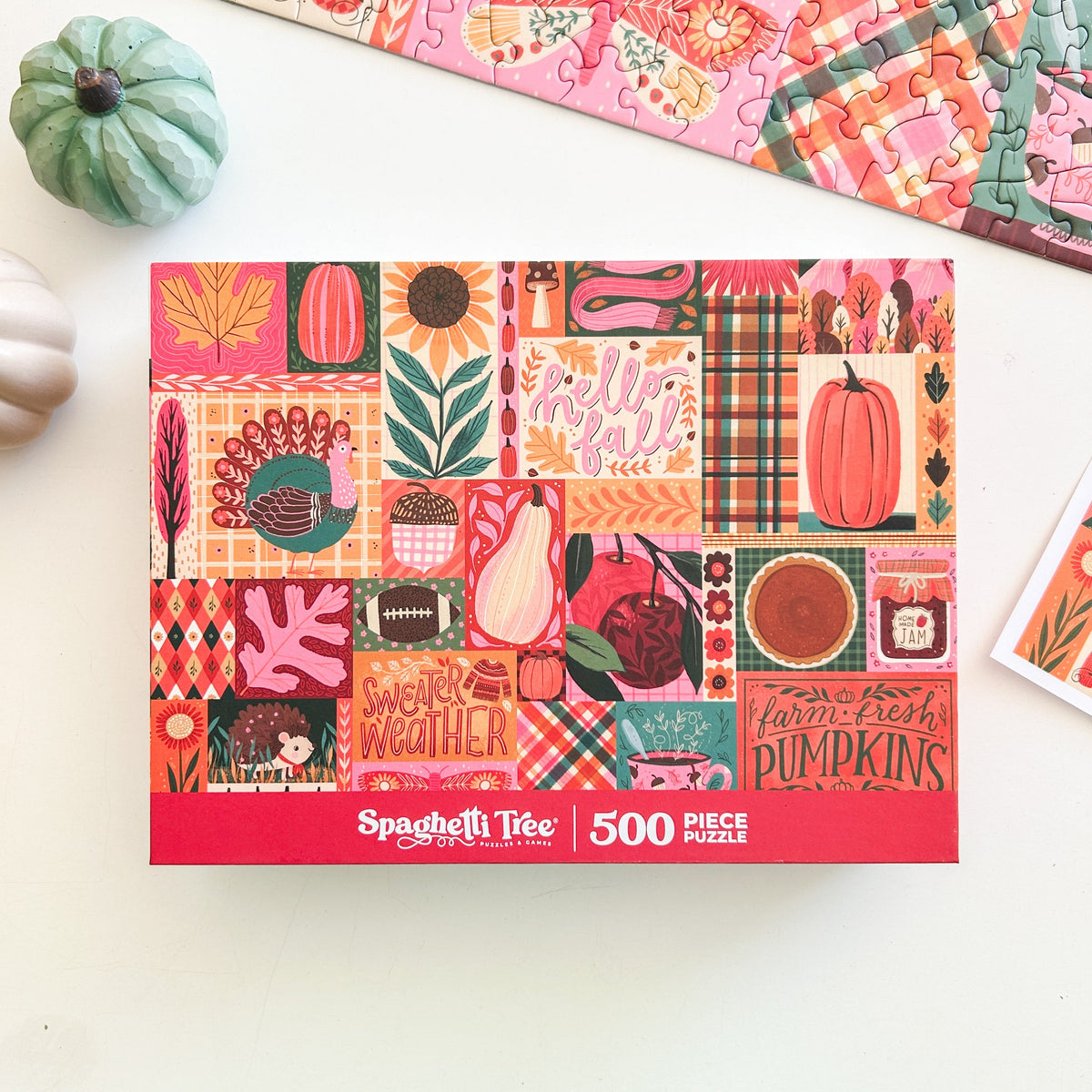 Above view of puzzle. Patchwork style graphics of gourds, plaid, leaves, ect. In reds oranges and pinks. 